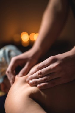 Erkek güçlü eller, mum ışığında orta yaşlı bir kadına masaj yapıyor.