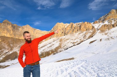 Kırmızı kazaklı ve kot pantolonlu sakallı, çekici beyaz bir adam kışın elini dağlara uzatarak destansı kayaların arkasını işaret ediyor. Turizm ve seyahat aşkı