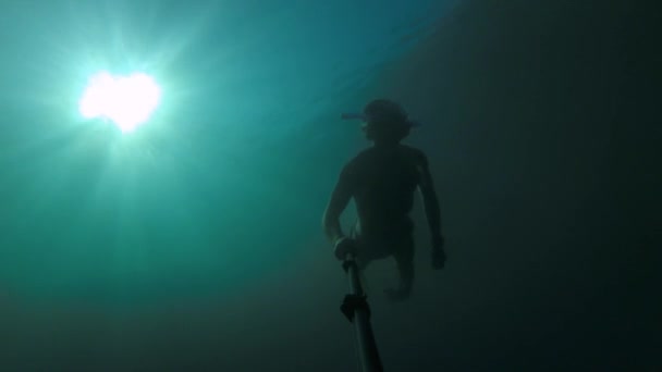 Un jeune sportif masqué et un tuba nagent avec un selfie stick profond sous l'eau. Éblouissement du soleil à travers l'eau — Video