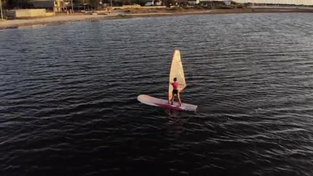 Vista aérea de uma jovem esportiva aprendendo a pilotar uma prancha de windsurf. Treino ao pôr-do-sol. Tecla baixa — Vídeo de Stock