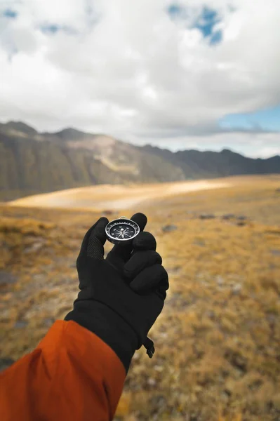 First-person view of a male travelers hand holding a magnetic compass against the backdrop of a mountainous area. Orientation and finding your way