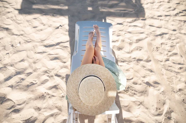 Top view of slender young caucasian woman in hat resting on the sandy beach on a sunny day. Slender legs and a hat on a sand background