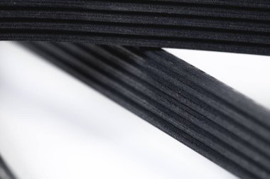 Gri arkaplanlı, sığ bir alan derinliğindeki bir jeneratörün polimer V-kuşağına yakın çekim. Otomatik parçaların lastik ürünleri için arkaplan