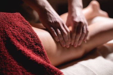 Masör, masaj salonunun karanlık bir odasında bayan bir sporcunun müşterisine bacak masajı yapıyor.