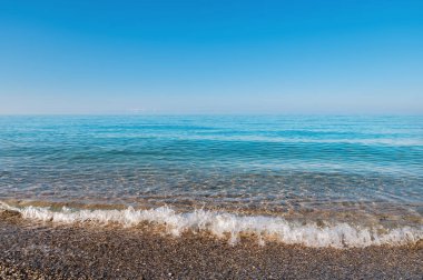 Sahilde sakin dalgalar hareket ediyor. Yüzeyinde sis olan sabah denizinin mavi dalgaları. Sabah denizi derinliği yok
