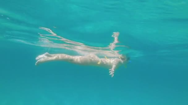 Uma jovem esbelta nada com uma máscara de mergulho e snorkel subaquático em um mar transparente com um fundo arenoso — Vídeo de Stock