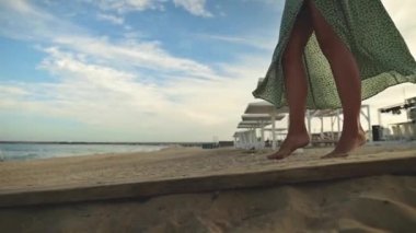 Sabahın erken saatlerinde denize yakın ıssız bir plaj boyunca çıplak ayakla dolaşan yeşil elbiseli, çekici, beyaz tenli genç bir kadın. Yavaş çekim