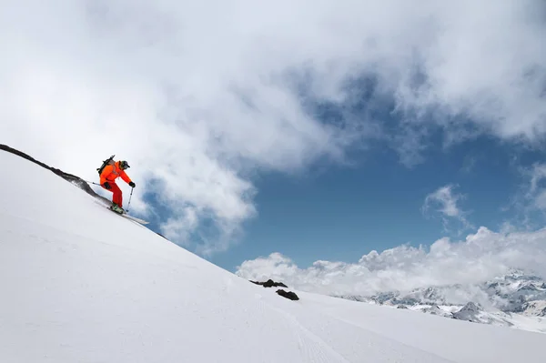 Skier in bright clothes quickly descends the mountain through the snow — Stock Photo, Image