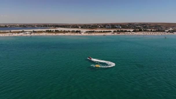 Vista aérea de tubos remolcados inflables para rodar turistas en un tubo atado a jetski a través del mar azul en un día soleado — Vídeo de stock