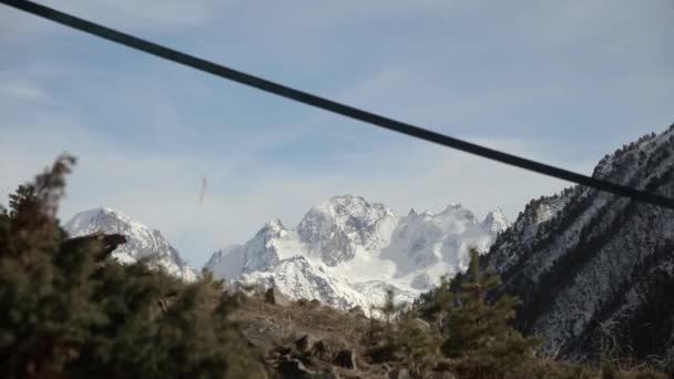 Za slunečného dne se ve větru houpal slackline mezi stromy vysoko v horách. Zasněžené hory v pozadí. Příprava na procházku po slackline — Stock video