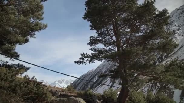 Um slackline sling balançando no vento entre árvores altas nas montanhas em um dia ensolarado. Montanhas cobertas de neve no fundo. Preparando-se para caminhar no slackline — Vídeo de Stock