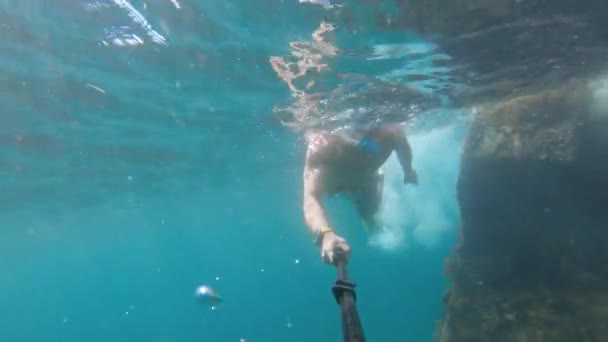 Un homme athlétique caucasien avec un bâton de selfie plonge dans l'eau de mer claire près de l'épave. Navire coulé couvert d'algues — Video