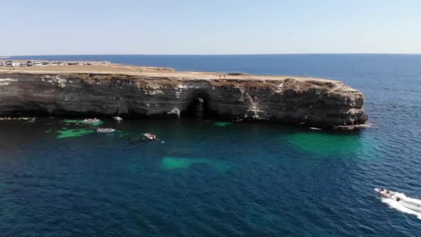 Veduta aerea di un volo vicino a un promontorio roccioso sotto il quale navigano le barche turistiche. Turisti e auto parcheggiate si trovano sulla riva. Turistico luoghi accessibili concetto — Video Stock