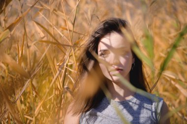 Üzgün ve düşünceli bir ifadeye sahip çekici bir beyaz kadın güneşli bir günde sazlıklar arasında duruyor. Saha kadınının derin, yaratıcı portresi.