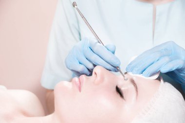 Yakın plan, güzel beyaz kadın salonda yatıyor, güzellik uzmanı eldivenli bir aletle kozmetik işlemler yapıyor.