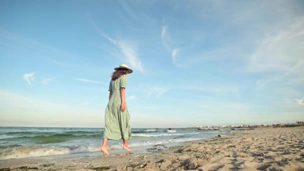 Привлекательная женщина в замедленной съемке гуляет босиком по пляжу ранним утром. Турист в светло-зеленом платье на золотом пляже — стоковое видео