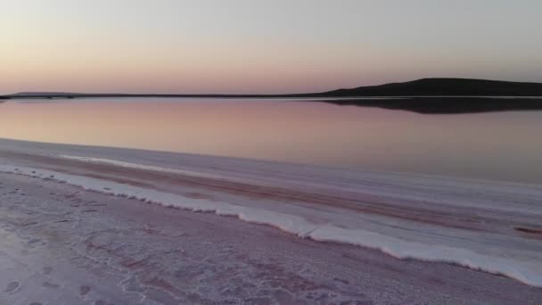 Luchtfoto van het vliegen over de zoute oever van roze zoutmeer in de avond bij schemering, blauwe lucht reflectie in roze water — Stockvideo