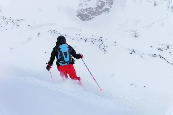 Een jonge vrouwelijke skiër rijdt in slecht zicht op een besneeuwde berghelling. Slecht weerski concept Achteraanzicht — Stockfoto