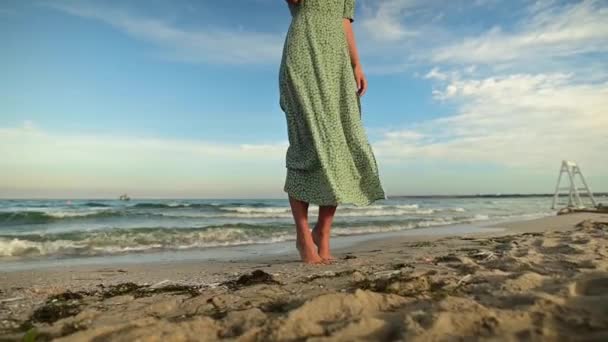 Крупным планом босые ноги Привлекательная кавказская стройная молодая женщина в зеленом платье рано утром прогуливается по пустынному пляжу у моря. Медленное движение. — стоковое видео
