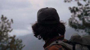 Dağların bulutlu havasında, akşamları ormandan çıkan, uzun saçlı, şapkalı genç bir adamın yakın görüntüsü. Seyahat ve seyahat.
