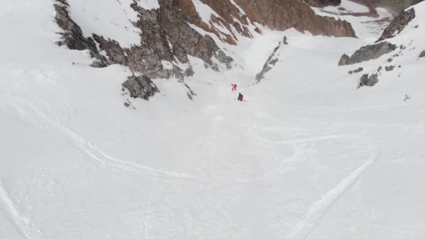 Δύο αθλητές σκιέρ και snowboarder κατεβαίνουν freeride κατά μήκος του couloir ψηλά στα βουνά στα τέλη της άνοιξης, κορυφαία θέα. Εναέρια πλάνα — Αρχείο Βίντεο