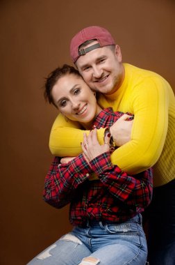 Beyaz tenli evli çift, sarılıyor ve öpüşüyorlar. Sıradan bir 30 yıllık stüdyo fotoğrafının günlük tarzı ve parlak giysileri.