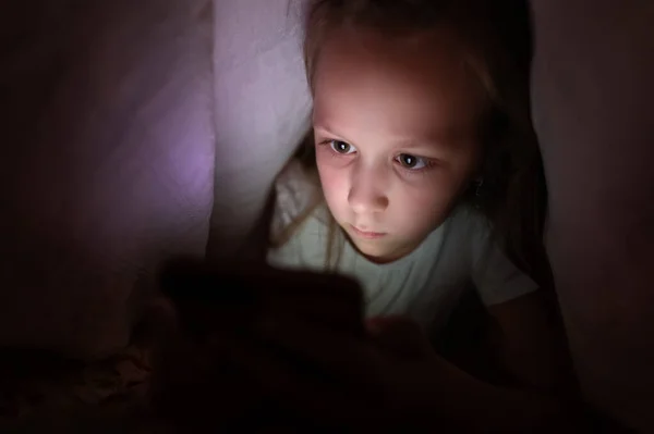 Gece yatağın altındaki battaniyenin altında video akıllı telefonu izleyen çocuklar ekrandan yansıyan ışıklar, bağımlılık oyunları ve çizgi film konsepti kullanırlar. — Stok fotoğraf