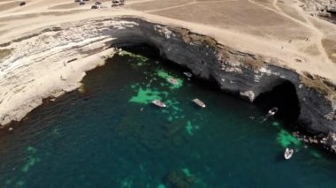 Turist teknelerinin yelken açtığı kayalık bir pelerinin yakınındaki bir uçuşun havadan görüntüsü. Turistler ve park etmiş arabalar kıyıda duruyor. Turistlere ulaşılabilir yer kavramı
