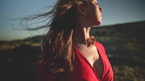 Närbild av en ung vit kvinna hår fladdrar i slow motion i vinden. Grunt skärpedjup. Flicka i röd klänning och hatt drömmare promenad vid havet — Stockvideo