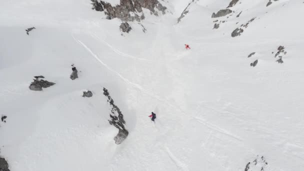 Zwei Sportler Skifahrer und Snowboarder fahren im späten Frühling Freeride entlang des Couloirs hoch in den Bergen, von oben gesehen. Luftaufnahmen — Stockvideo