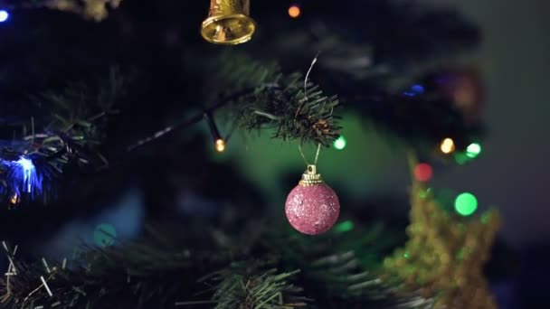 Um close-up de um brinquedo de Natal pesa em uma árvore de Natal com luzes piscantes de guirlandas no fundo. Profundidade rasa do foco flutuante do campo — Vídeo de Stock