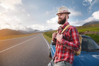 Mutlu sakallı adam, öğleden sonra dağların arkasında arabaya yaslanıyor.