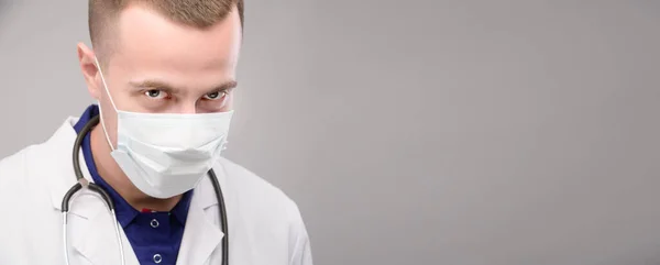 Panoramisch portret jonge blanke arts met een masker kijkt onheilspellend in de camera van onder zijn voorhoofd. Medisch samenzweringsconcept tegen de mensheid — Stockfoto