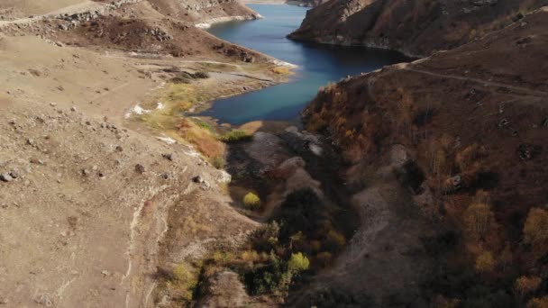 Vista aérea do voo sobre um lago alto da montanha cercado por rochas e colinas em um dia ensolarado — Vídeo de Stock