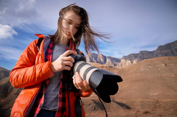 Молода хіпстерка з фотоапаратом в руках у горах підсвічується. Волосся трясеться на вітрі — стокове фото