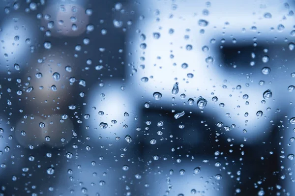 Капли воды на стекле в дождливую погоду с небольшими спальными районами на заднем плане. Осенний холодный влажный фон — стоковое фото