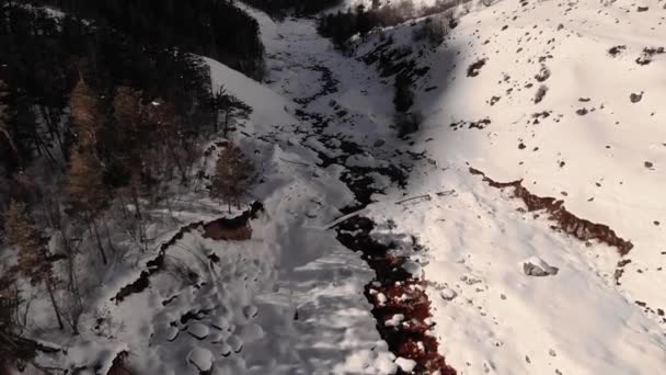 Зимний лес и заснеженная река с высоким содержанием железа в заносах белого снега высоко в горах в солнечный день. Вид с воздуха — стоковое видео