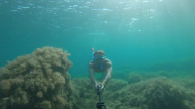 Deniz. Sualtı maskeli ve şnorkeli olan yüzgeçli bir adam selfie çubuğuyla denizde yüzüyor. Mısır. Bir aksiyon kamerasında sualtı dünyası