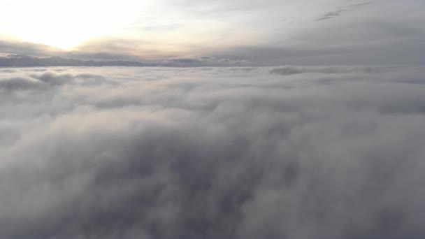 Increíble vista aérea sobre una niebla arremolinada y nubes al atardecer en las montañas. Volando sobre una superficie baja de nubes con una cresta en el fondo — Vídeos de Stock