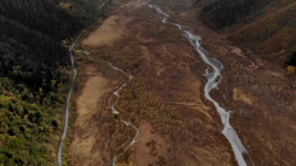 Een meanderende rivier die door een bergdal stroomt. Boven is er een pittoresk luchtlandschap van een smalle kronkelende rivier, naast een asfaltweg. De mooiste wegen ter wereld — Stockvideo