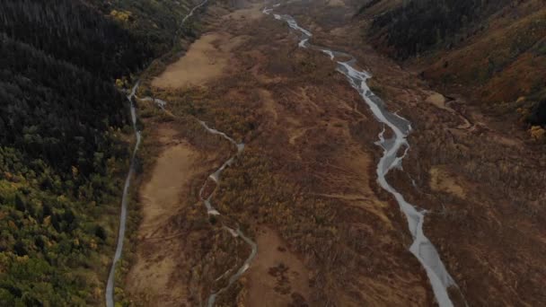 Um rio sinuoso que flui através de um vale de montanha. Acima, há uma paisagem aérea pitoresca de um estreito rio sinuoso, ao lado de uma estrada de asfalto. As estradas mais bonitas do mundo — Vídeo de Stock