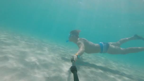 Deniz. Sualtı maskeli ve şnorkeli olan yüzgeçli bir adam selfie çubuğuyla denizde yüzüyor. Mısır. Bir aksiyon kamerasında sualtı dünyası — Stok video