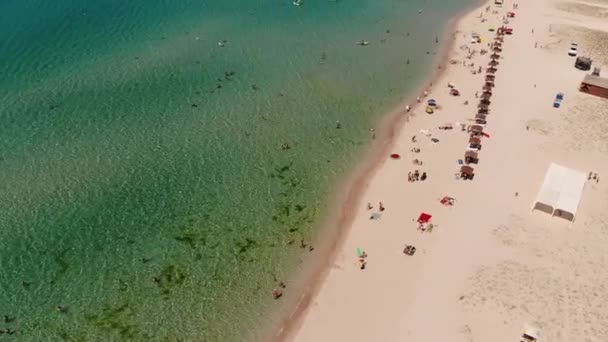 Вид с воздуха на лазурный пляж центральной Азии с отдыхающими туристами и пляжными зонтиками. Предпосылки для туризма и отдыха у моря — стоковое видео