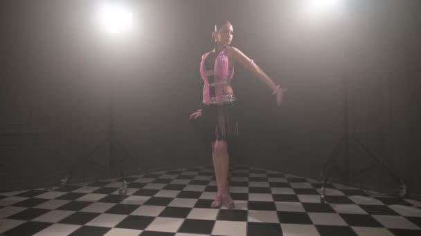 Привлекательная девушка-подросток в красивом розовом черном платье профессионально танцует бальные спортивные танцы самбу латиноамериканские танцы в темной комнате наполненной дымом — стоковое видео