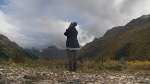 Jonge blanke vrouw maakt foto 's op haar smartphone in de bergen. Prachtig panorama van hoge epische kliffen en bergtoppen op een herfstbewolkte dag — Stockvideo