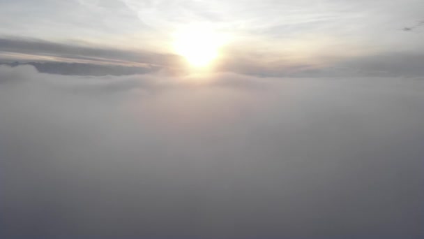 Increíble vista aérea sobre una niebla arremolinada y nubes al atardecer en las montañas. Volando sobre una superficie baja de nubes con una cresta en el fondo — Vídeos de Stock