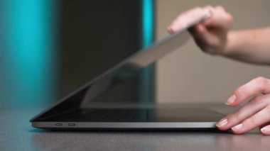 Genç beyaz bir kadının elleri mavi bir arka ışığa karşı gri bir dizüstü bilgisayar açıyor. Sığ alan derinliği