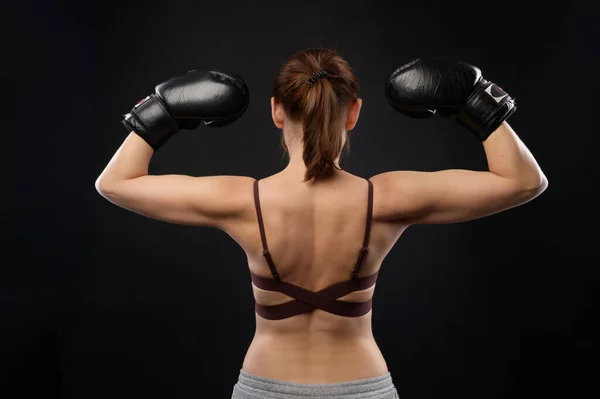 Ritratto di una donna pugile con la schiena. La donna caucasica con i guanti da boxe mostra un gesto di forza. Studio foto — Foto Stock