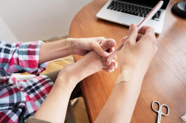 Primer plano de una mujer con ropa casual sentada a la mesa haciendo una pedicura sola en casa — Foto de Stock