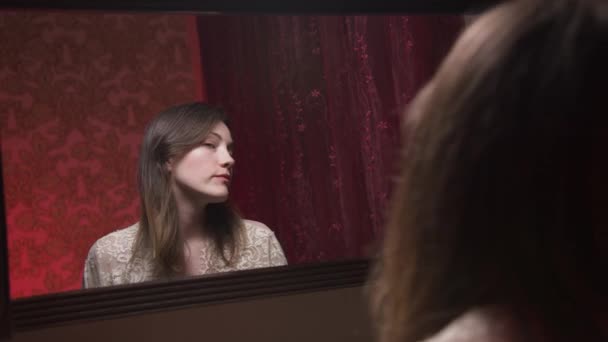 Giovane donna caucasica attraente dipinge labbra di fronte a uno specchio in una camera da letto la sera. Preparazione della festa. Applicare il trucco — Video Stock